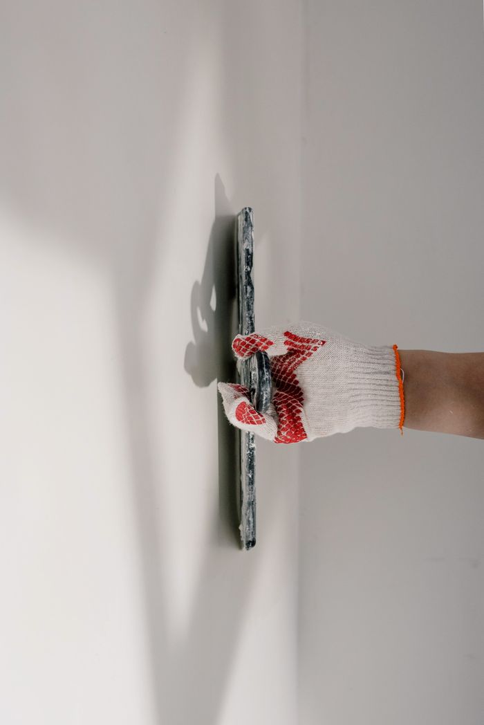 Crop anonymous painter in gloves preparing wall for painting works during renovation process in apartment