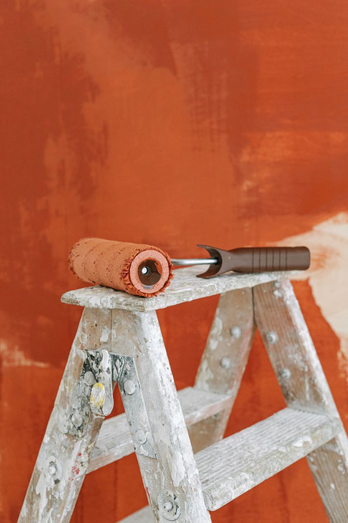 A paint roller on a stepladder against a partially painted wall, signifying home improvement.